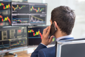 bond-corporate-actions.jpg. Alt attribute: “man on the phone in front of 4 monitors displaying corporate bonds action